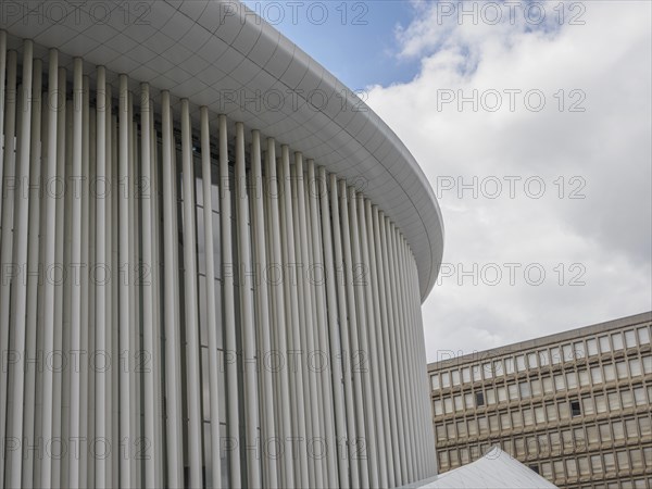 Part of a modern building in Luxembourg with vertical columns and a slightly cloudy sky in the background, modern buildings with trees and glass facades, luxembourg