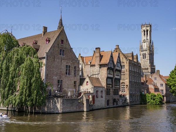 Historic buildings with red tiled roofs and a high tower on a river under a blue sky, historic houses and churches with towers on a river in Belgium, Bruges, Belgium, Europe