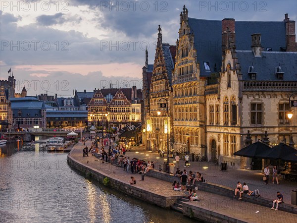 Bruges street scene with busy harbour, historic buildings and people at dusk, historic buildings with towers and bridges on a river at blue hour, gent, belgium