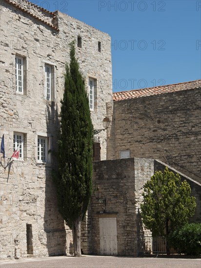 Historic stone building with cypress and flags, under a sunny sky, Provence, le Castellet, France, Europe