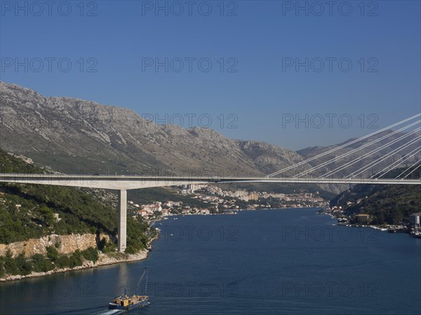 Wide view of a suspension bridge over a wide river, surrounded by a city and mountains under a clear sky, the old town of Dubrovnik with historic houses, churches, red roofs and fortress walls, dubrovnik, coratia