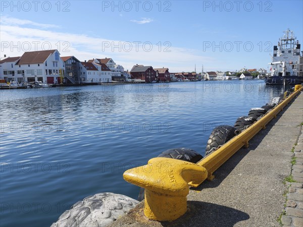 Waterfront with a yellow bollard and tyre protection, water and city in the background, in sunny weather, harbour in norway with boats, ships and many houses by the sea, Haugesund, Norway, Europe