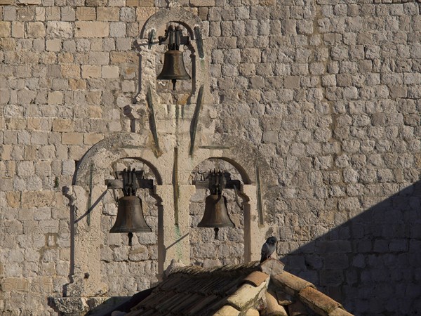 Historic bells on an old stone wall with a single bird on it in the afternoon sun, the old town of Dubrovnik with historic houses, churches, red roofs and fortress walls, dubrovnik, coratia