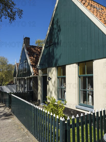 Traditional green houses with white fences along a street in a sunny village, Enkhuizen, Nirderlande