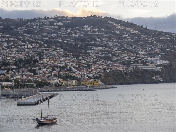 Coastal town at dusk, numerous houses stretch over the hill, a boat is visible in the water, Madeira, Portugal, Europe