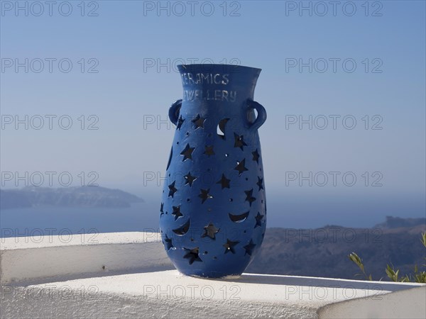 Blue vase with star and moon motifs on a white terrace with sea and mountain views in the background, The volcanic island of Santorini with blue and white houses and churches, flowers and palm trees on a volcanic island, santorini, greece
