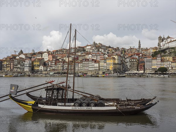 A traditional boat in still, murky water with a town and a hill in the background, Colourful houses on a river with colourful boats and a large bridge, porto, Portugal, Europe