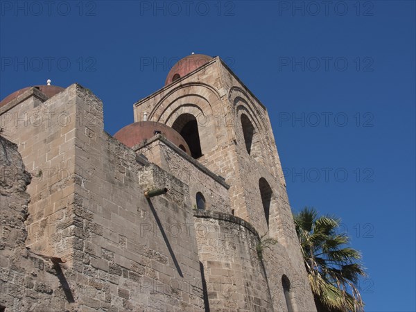 Historic church building with round towers, flanked by palm trees, under a clear blue sky, palermo in sicily with an impressive cathedral, monuments and old houses with balconies, palm trees and flowers in italy, palermo, sicily