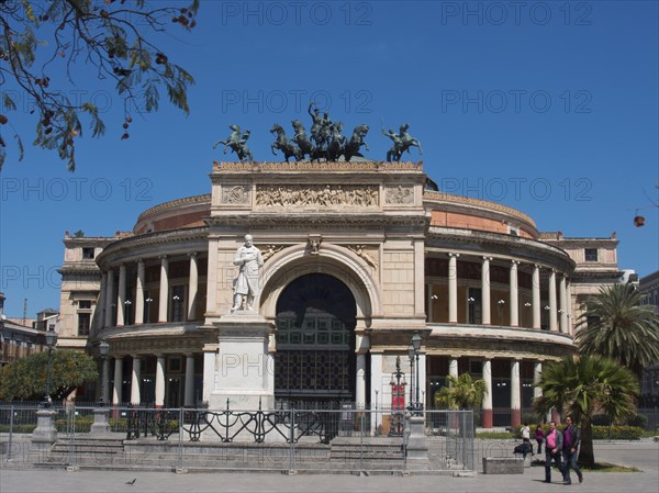 A large, round historical building with a statue and columns on a sunny square, palermo in sicily with an impressive cathedral, monuments and old houses with balconies, palm trees and flowers in italy, palermo, sicily