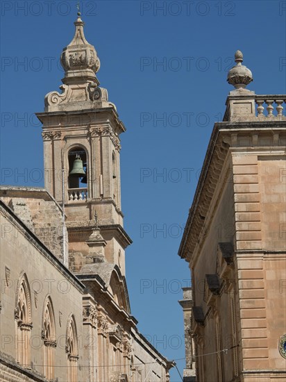 A tower with bell and adjoining building under a blue sky, the town of mdina on the island of malta with historic houses, colourful balconies, magnificent churches, mdina, Malta, Europe