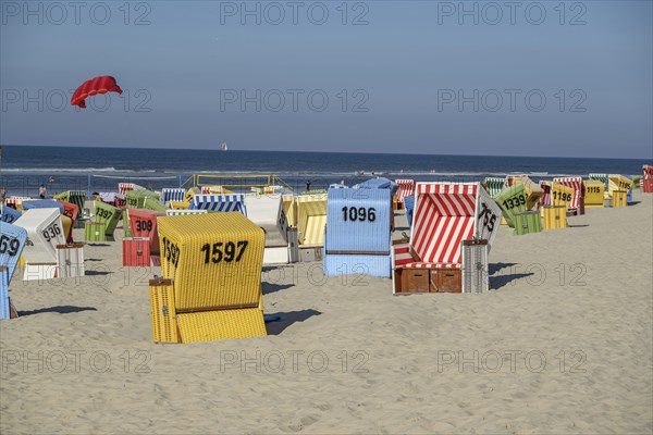 Colourful beach chairs on the sandy beach, a red kite flying, calm sea scenery under a clear sky, summer evening on the beach with green dune grasses against a blue sky and colourful beach chairs, langeoog, germany