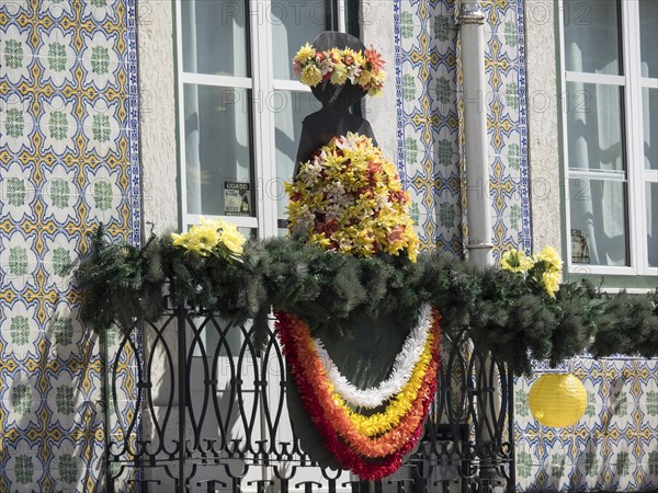 Colourful floral decoration on an ornate balcony with statue and tiles in the background, Lisbon, Portugal, Europe
