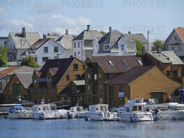 Many boats are docked in front of traditional wooden houses on a sunny day next to the water, harbour in norway with boats, ships and many houses by the sea, Haugesund, Norway, Europe