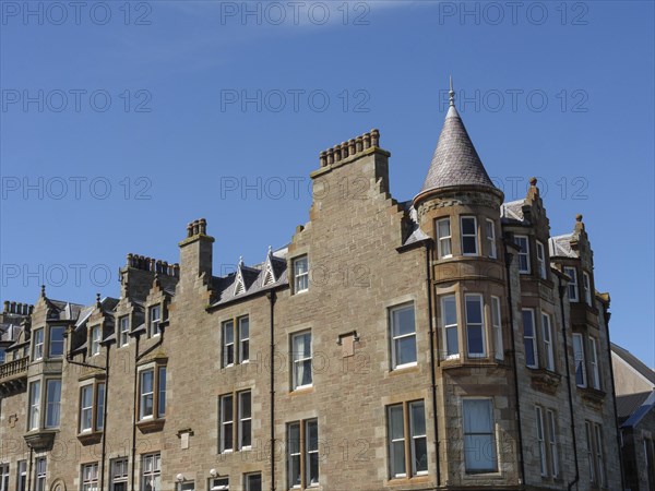 Tall historic building with many chimneys and a prominent tower under a clear blue sky, grey houses with colourful flags in a seaside town, Lerwick, Scotland, United Kingdom, Europe
