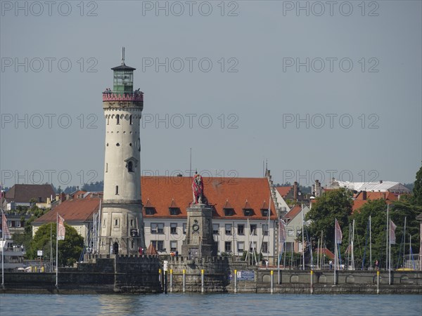 A lighthouse and a statue at the harbour, surrounded by historic buildings and water, view of a town at the lake with lighthouse and church towers, Lindau, Germany, Europe