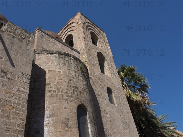 Historic church building with round towers and palm trees in the sunshine, palermo in sicily with an impressive cathedral, monuments and old houses with balconies, palm trees and flowers in italy, palermo, sicily