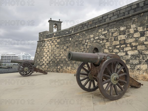 Two old cannons in front of the stone walls of a fortress under a cloudy sky, Lanzarote, Spain, Europe
