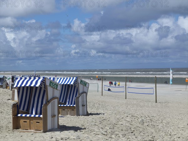 Blue and white beach chairs on the beach with people in the background in sunny weather, clouds on the beach of Noderney in front of colourful beach chairs and waves in the sea, Nordereney, Germany, Europe