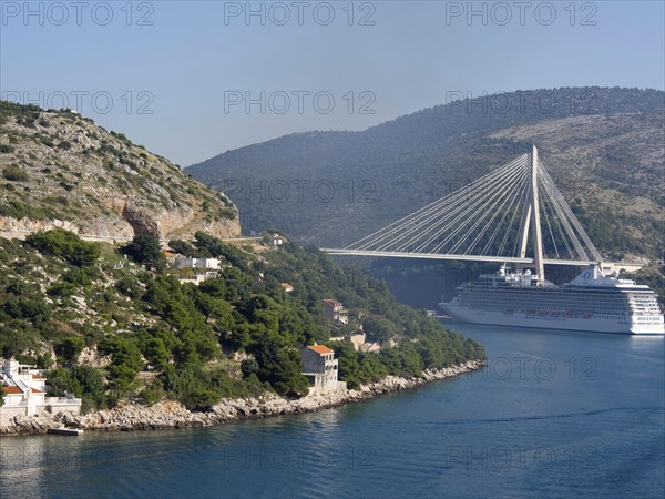 View of a coastline with green hills, a bridge and a cruise ship under a clear blue sky, the old town of Dubrovnik with historic houses, churches, red roofs and fortress walls, dubrovnik, coratia
