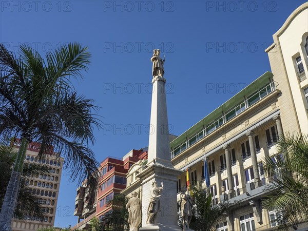 Monumental statue between palm trees and historic buildings under a blue sky, Tenerife, Spain, Europe