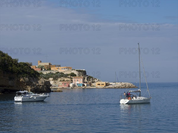 Sailing boats in front of a coastal landscape with cliffs and small houses under a partly cloudy sky, Marseille on the Mediterranean Sea with the old cathedral and ships in the historic harbour, rocky coast on the Mediterranean Sea, marseille, france