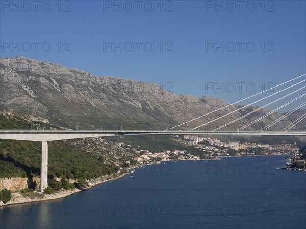 Wide angle shot of a bridge connecting a coastal town with houses and mountains, the old town of Dubrovnik with historic houses, churches, red roofs and fortress walls, dubrovnik, coratia