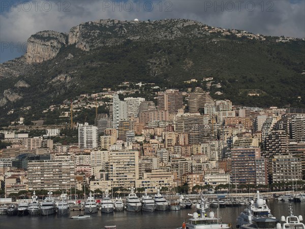 Large city with skyscrapers on a green hill and boats in the foreground under a cloudy sky, monaco on the French Mediterranean coast, harbour against an imposing city backdrop and historic buildings, Monte Carlo, Monaco, Europe