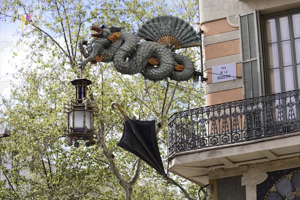 Barcelona, Catalonia, Spain, Europe, Dragon statue carrying a decorative lantern and an umbrella in front of a balcony, Europe