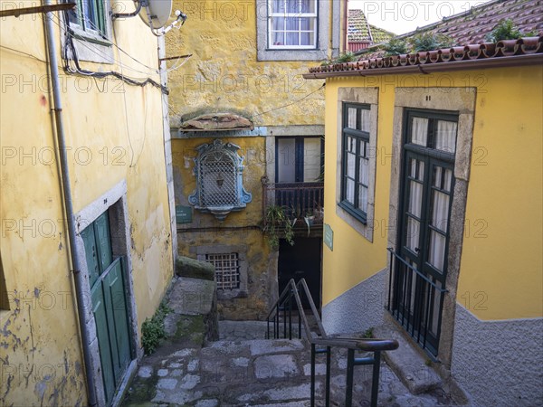 Narrow alley with yellow buildings, windows, doors and a staircase in an urban environment, old houses in the historic centre of Porto on the Douro, Porto, portugal