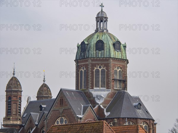 A church building with a central green dome and two smaller towers, under a cloudy sky, historic houses in Hoorn and ships in the harbour, hoorn, the netherlands