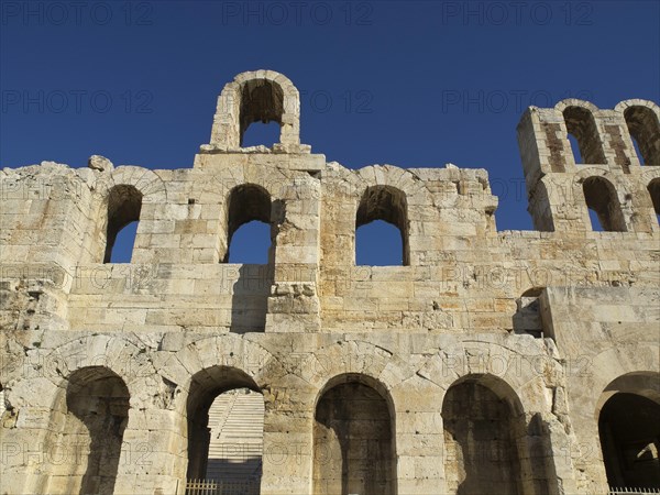 Ancient stone structure with multiple arches under a clear blue sky, Ancient buildings with columns and trees on the Acropolis in Athens against a blue sky, athens, greece