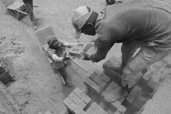Child handing a brick to a man in a dusty construction site in black and white, Jammu and Kashmir, India, Asia