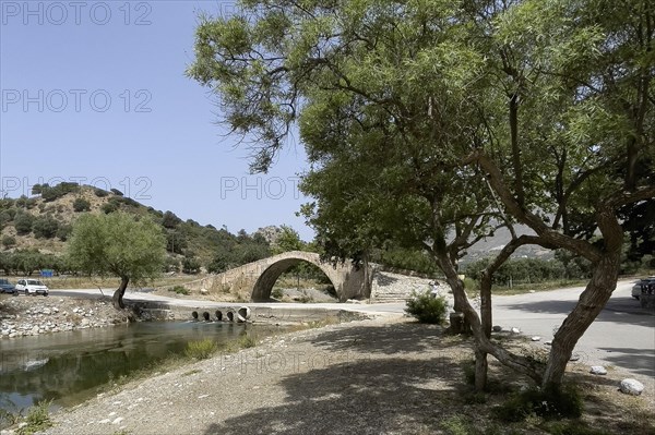 Historic classical arch bridge made of stone in Venetian architectural style Venetian Great Old Bridge 19th century stone bridge built in 1850 in Ottoman times over the middle reaches of the Megalopotamos River near Preveli, in front of it modern flat river crossing with concrete pipes Tubes for water flow, Agios Vasilios, Crete, Greece, Europe