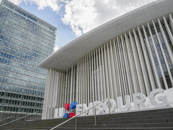 Modern building in Luxembourg with glass facade and striking columns next to a skyscraper, under a slightly cloudy sky, modern buildings with trees and glass facades, luxembourg