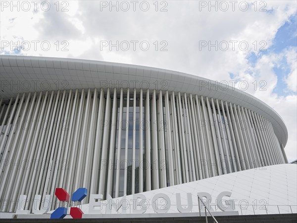 Large modern building in Luxembourg with glass facade and vertical columns under a slightly cloudy sky, modern buildings with trees and glass facades, luxembourg