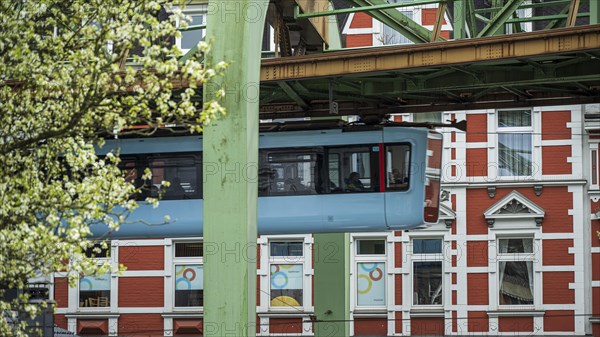 Suspension railway passes a red and white building surrounded by blossoming trees in Wuppertal Vohwinkel
