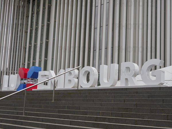 Stairs in front of a modern building in Luxembourg with large lettering and columns, modern buildings with trees and glass facades, luxembourg