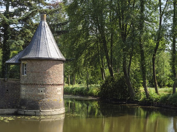 Round tower on a moat with a reflecting water surface, surrounded by summer trees and a peaceful atmosphere, ochtrup, münsterland, germany