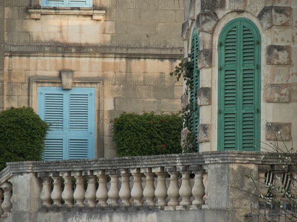 Close-up view of a building with green shutters, balcony railings and landscaped garden, valetta, mediterranean sea, malta