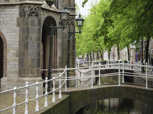 Historic buildings and lanterns along a bridge over a canal with green trees, Delft, Holland, Netherlands