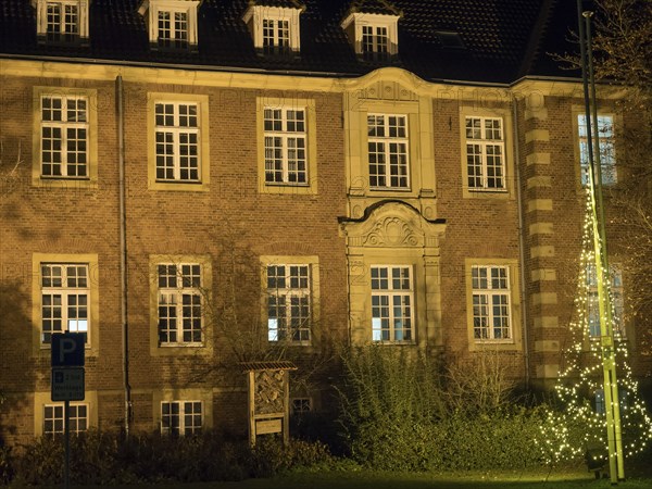 A historic building with illuminated windows at night. The warm light emphasises the details of the architecture, Borken, Münsterland, North Rhine-Westphalia, Germany, Europe