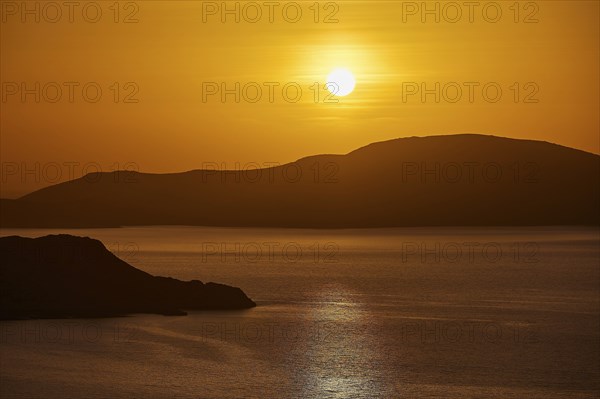 The sun sets over a calm sea and rolling hills, bathing the scene in warm orange, Makri Island, Alimia Island, Kritinia Castle, St John's Castle, Kritinia, Rhodes, Dodecanese, Greek Islands, Greece, Europe