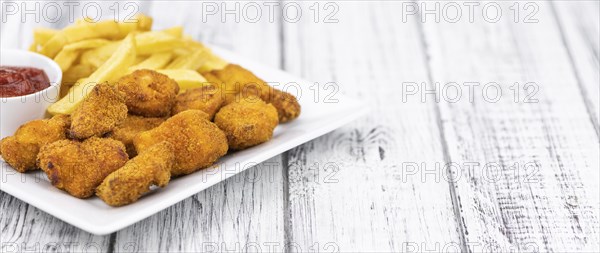 Vintage wooden table with fresh made Chicken Nuggets (close-up shot, selective focus)
