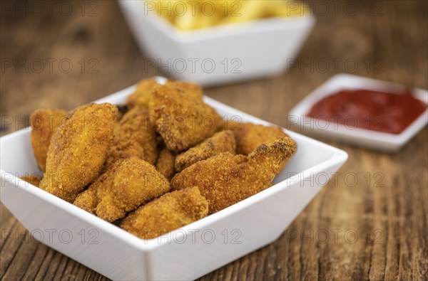 Vintage wooden table with fresh made Chicken Nuggets (close-up shot, selective focus)