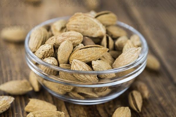Roasted Almonds (in shell) on an old wooden table (close-up shot, selective focus)