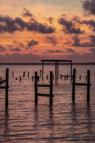 Sunset behind remains of damaged wooden pier pilings on Perdido Bay in Perdido Key, Florida