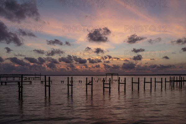 Sunset behind remains of damaged wooden pier pilings on Perdido Bay in Perdido Key, Florida