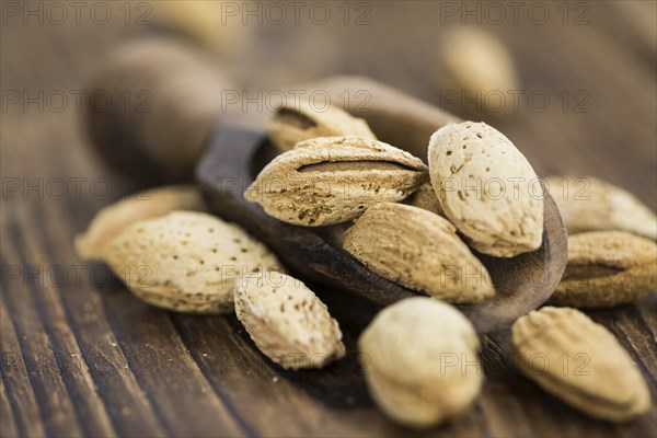 An old wooden table with roasted Almonds (in the shell) as detailed close-up shot (selective focus)