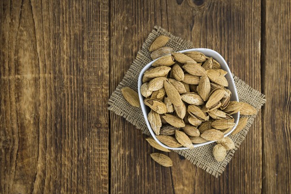 An old wooden table with roasted Almonds (in the shell) as detailed close-up shot (selective focus)