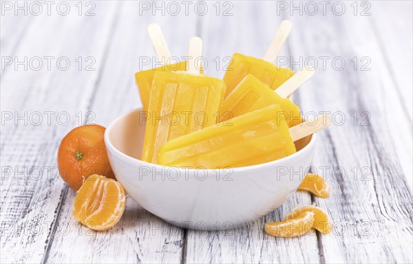 Portion of fresh homemade Tangerine Popsicles (close-up shot, selective focus) on a vintage background